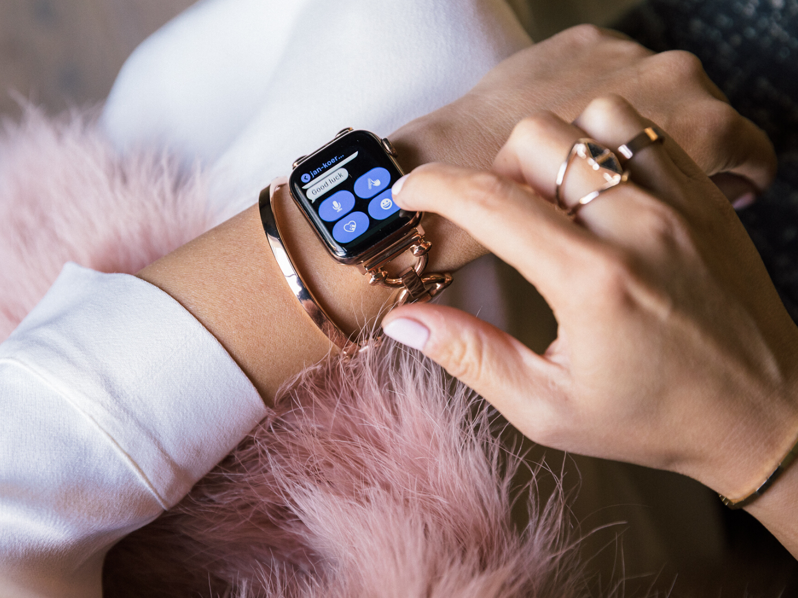 Woman writing a test message on her rose gold Apple Watch, wearing Goldenerre rose gold classic link watch band, rose gold bangle, and rose gold rings