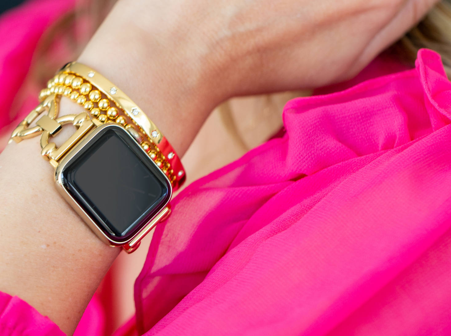 gold apple watch band with gold stacking bracelets and pink shirt