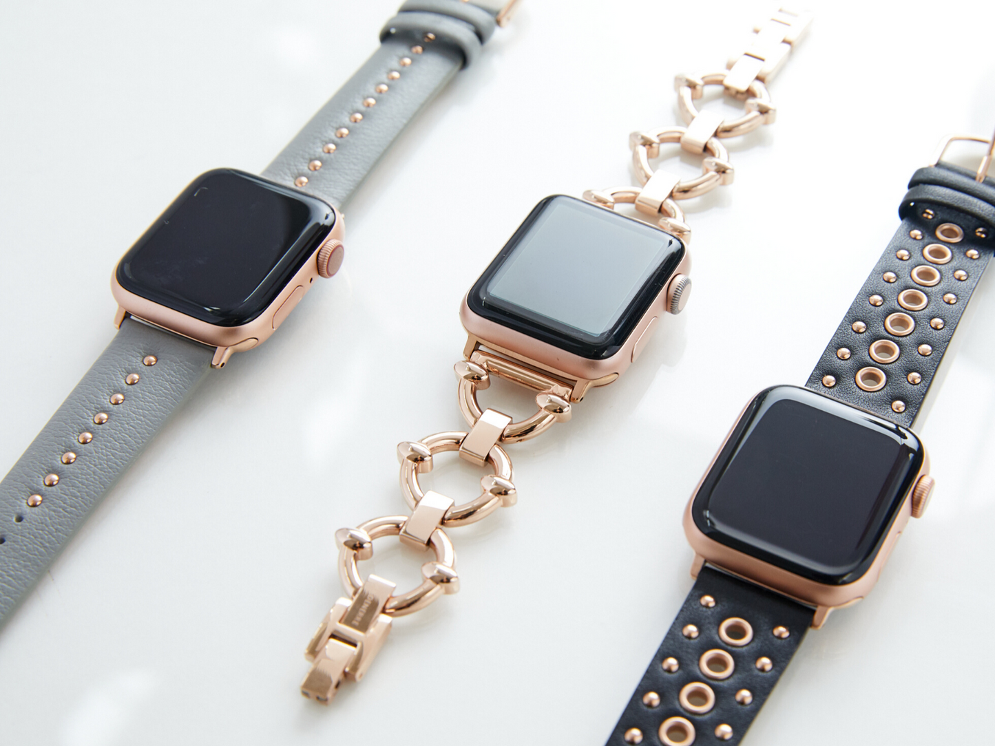 Trio of rose gold Apple Watch bands, shown from left to right with silver mini stud band, rose gold classic link bracelet for the Apple Watch, and grommet stud band for the Apple Watch, all by Goldenerre