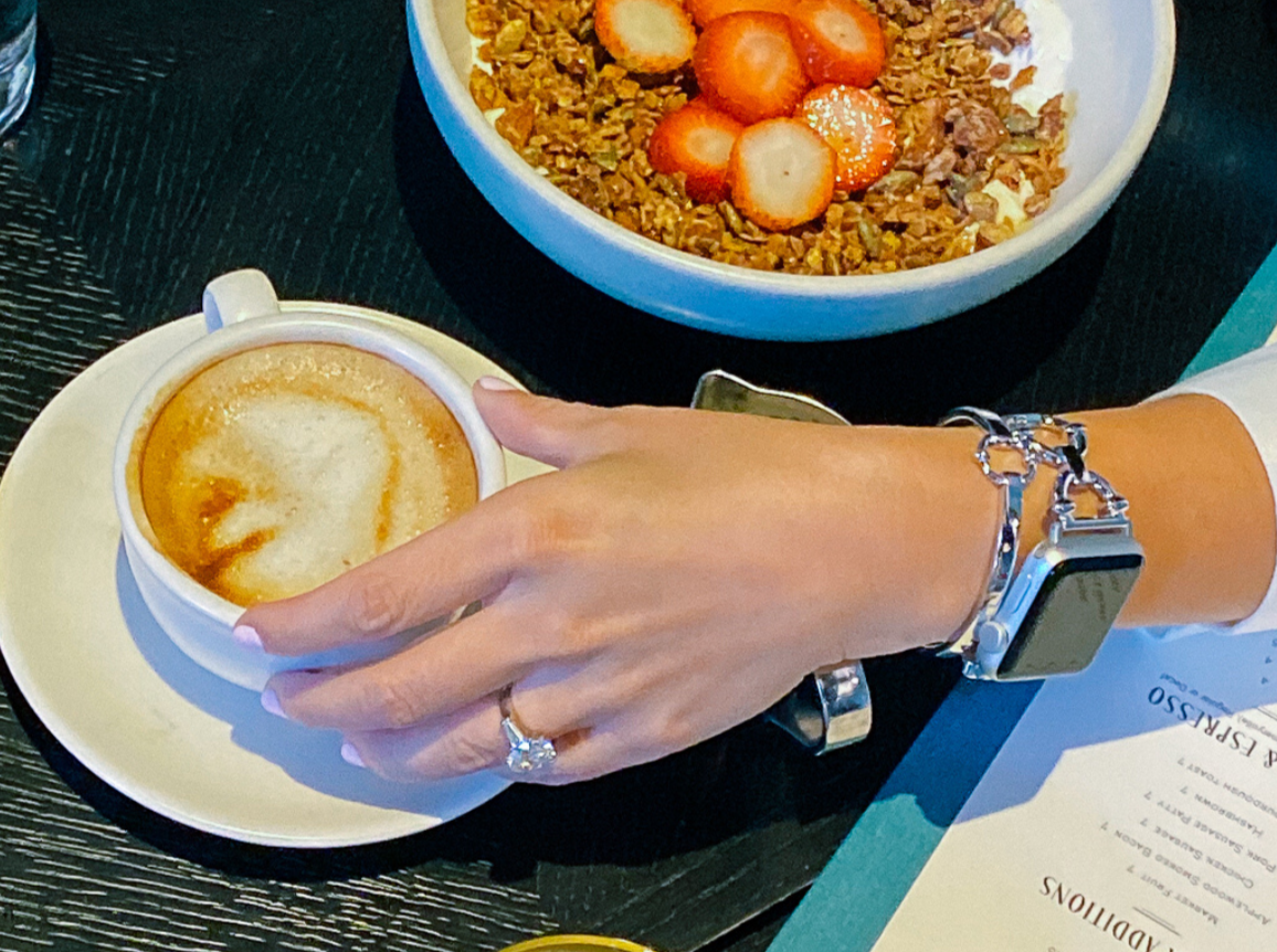 Woman wearing silver classic link bracelet for the Apple Watch, at breakfast with a cup of coffee