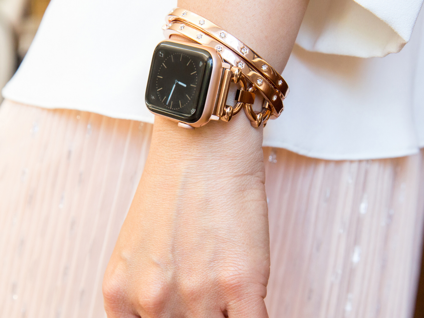 Woman with wrist by side, showing rose gold apple watch with Goldenerre rose gold classic link bracelet and two rose gold rhinestone bangles